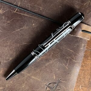 A thick bodied twist pen in dark chrome and black and white colors on a leather journal