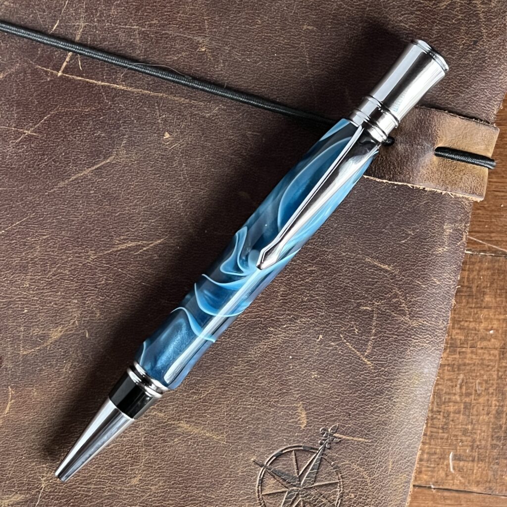 Blue and white swirled resin executive pen with chrome finish laying on a brown leather journal